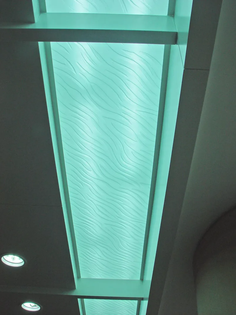Backlit wave-pattern decorative glass ceiling panels in recessed coffers with teal LED lighting
