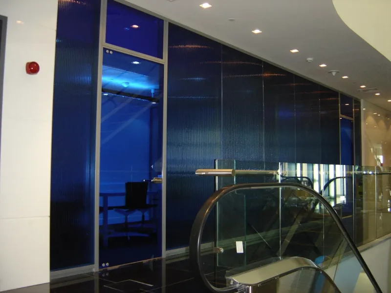 Blue reeded glass office partition with a framed glass door beside an escalator