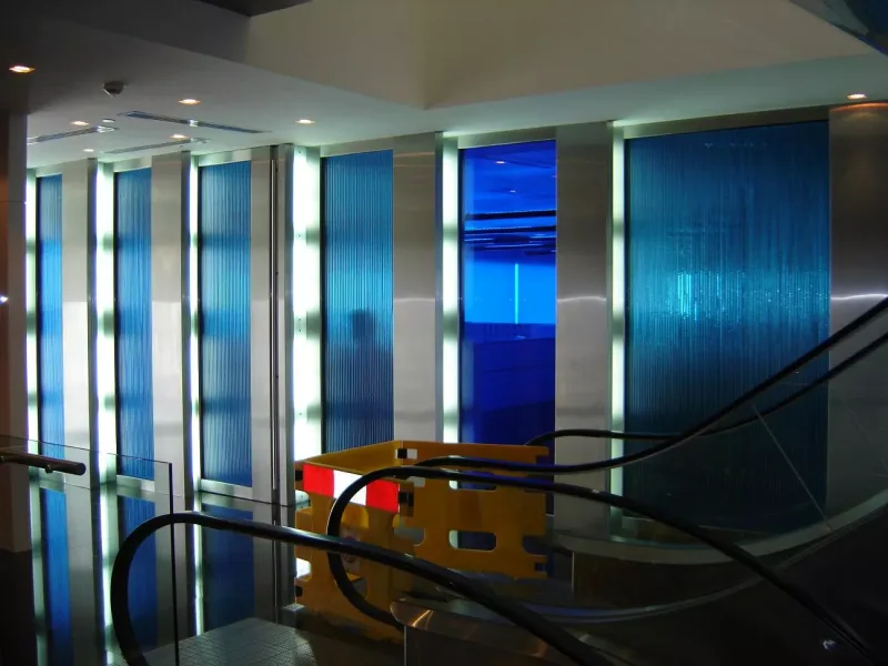 Blue reeded glass wall panels in stainless steel frames with backlit strips in a commercial lobby
