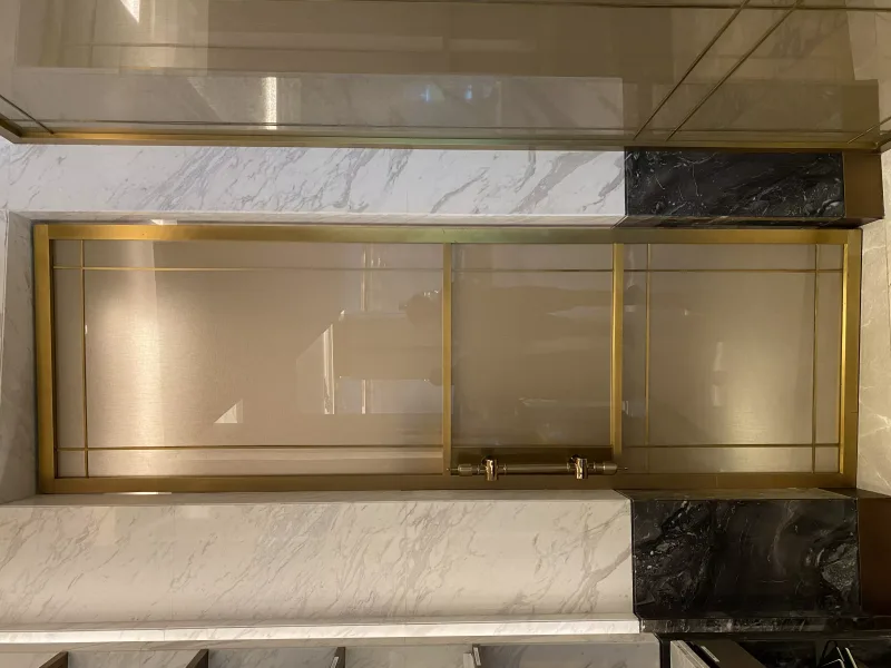 Brass-framed tinted glass door with brass pull handle in a marble surround