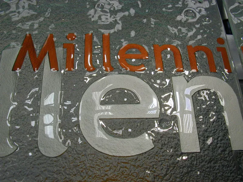 Dark cast glass logo plaque with embossed lettering and a circular emblem