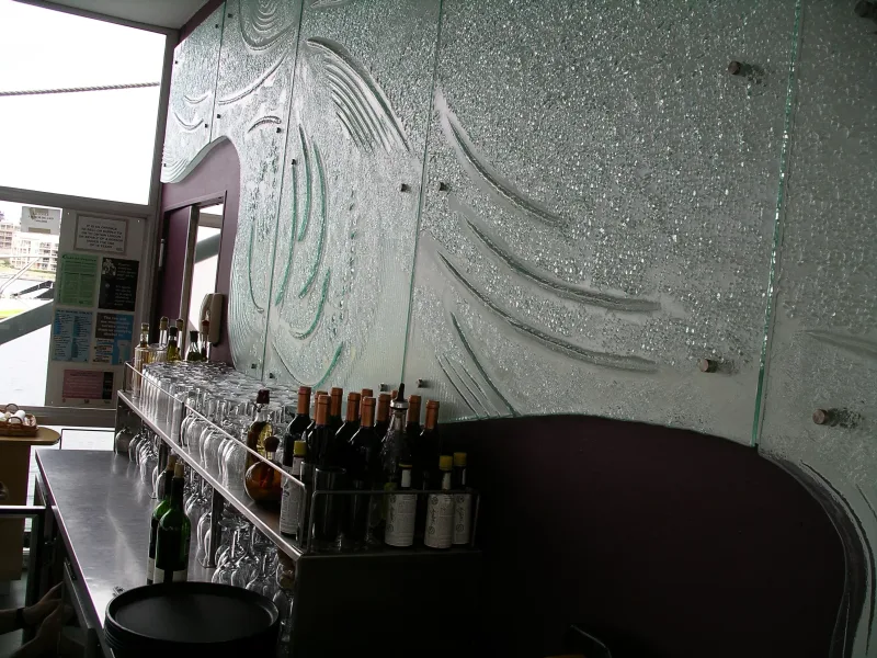 Cast glass wall with wave relief pattern and copper standoffs behind a bar counter