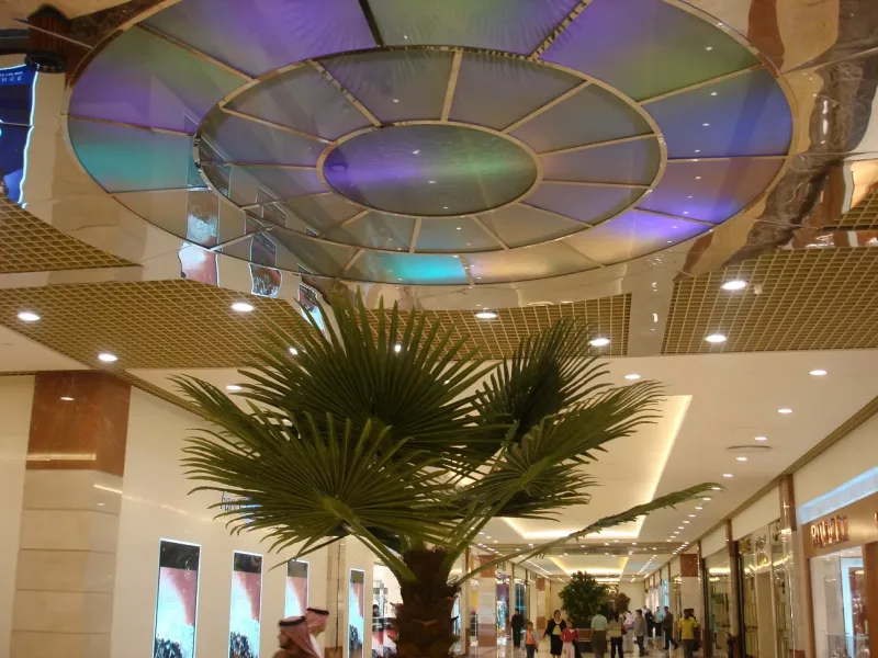 Circular backlit glass ceiling feature above a shopping mall corridor with a palm tree