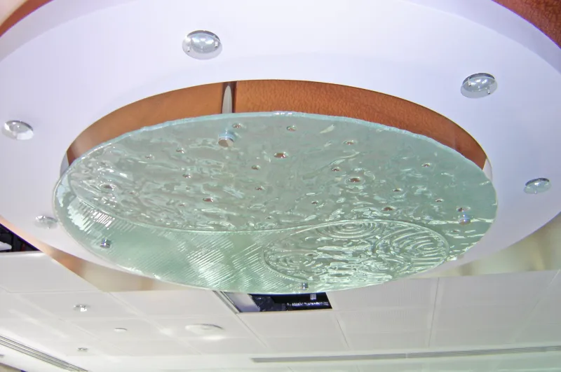 Close-up of a circular textured glass ceiling disc with water-ripple relief and stainless standoff fixings