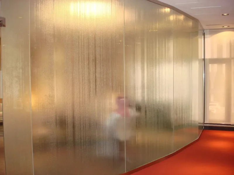 Curved textured glass partition wall along an office corridor with red carpet