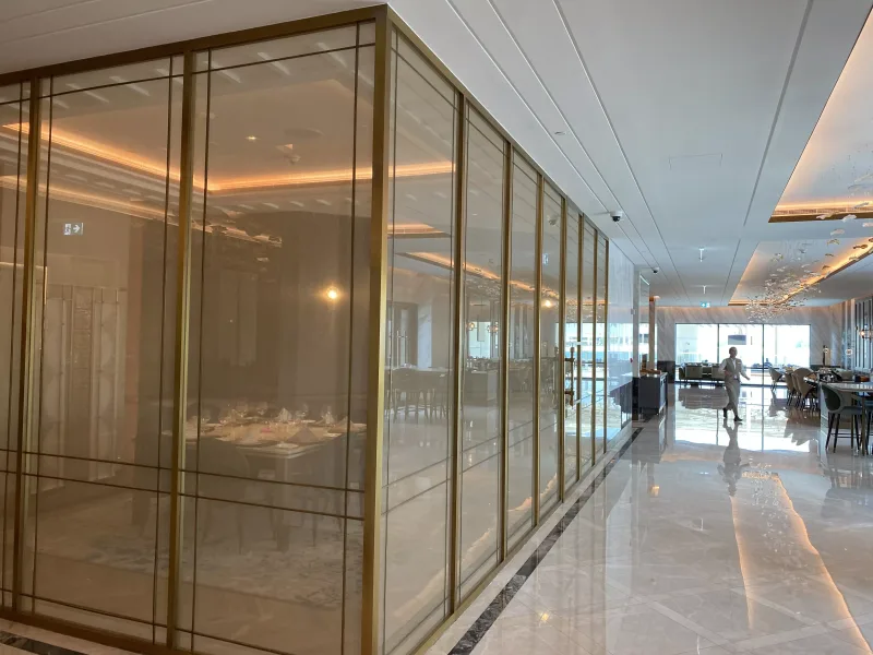Floor-to-ceiling brass-framed glass wall with grid lines along a restaurant corridor