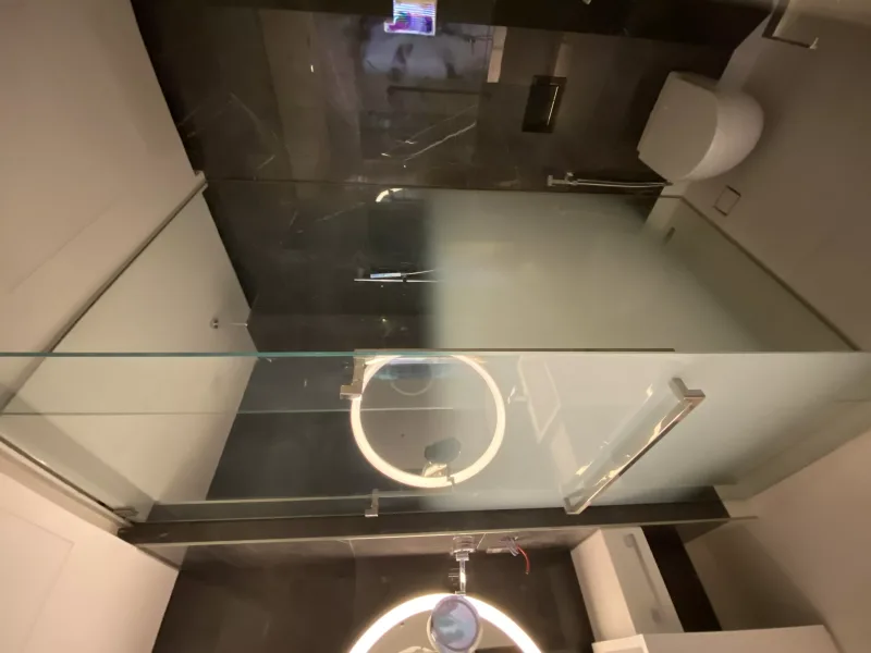 Frosted glass shower enclosure with square chrome pull handle in a black marble bathroom