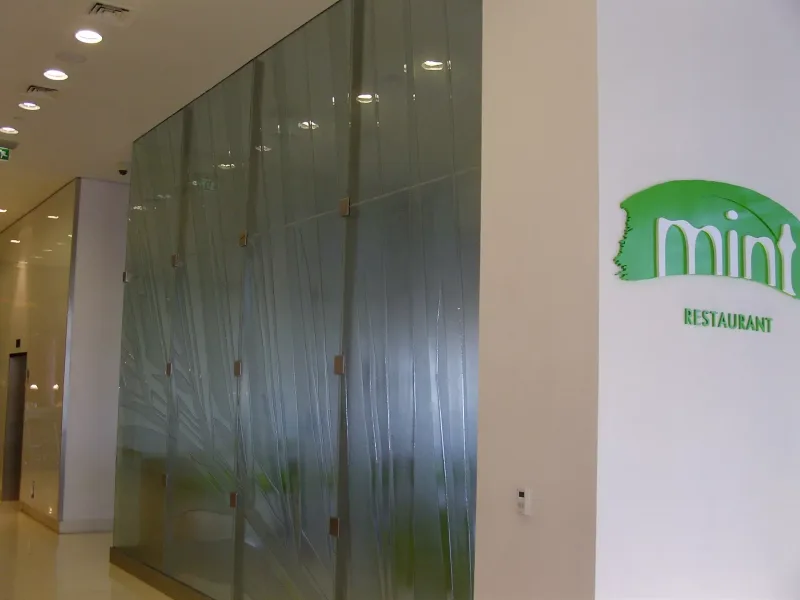 Leaf-pattern relief glass partition wall at a restaurant entrance with steel fixings