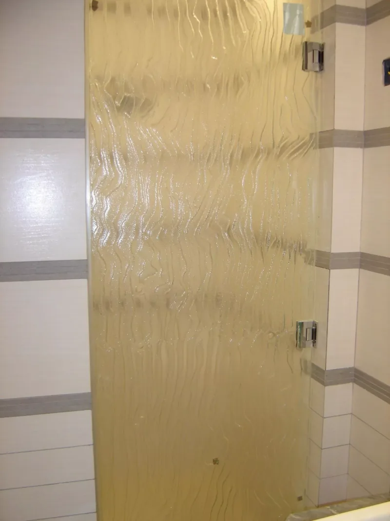 Rippled textured glass shower door with chrome hinges in a tiled shower