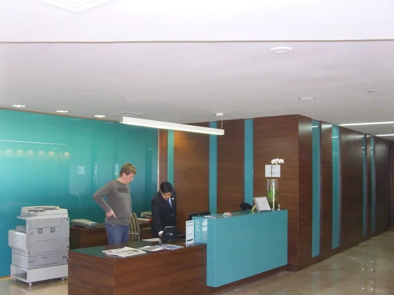 Turquoise back-painted glass wall and reception desk panels with timber veneer in an office lobby